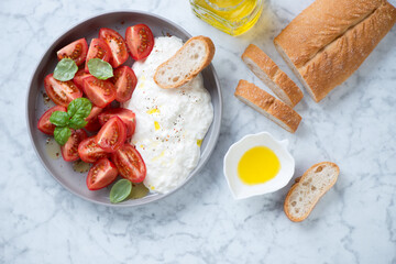 Salad with red cherry tomatoes and stracciatella cheese, flatlay over light-grey marble background, horizontal shot
