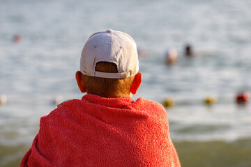 a boy wrapped in a red blanket looks at the sea