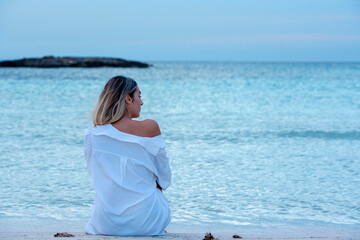 Woman on the beach of Formentera with white shirt at sunset.