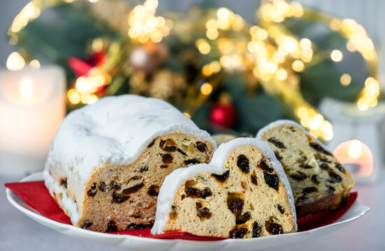 Traditional festive European pastry with raisins, nuts, candied fruit and icing sugar. Christmas pie and warm bokeh lights on background. Homemade bakery, vegan dessert for winter holidays.