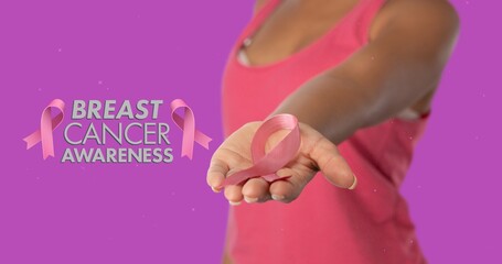 Composite image of woman showing breast cancer ribbon against purple background