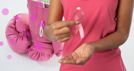 Midsection of woman holding breast cancer ribbon while boxing gloves in background