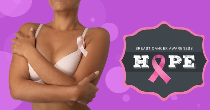 Composite image of woman in bra by hope text and breast cancer ribbon against purple background
