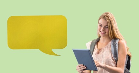 Digital composite of blank yellow speech bubble with copy space by smiling student using tablet pc