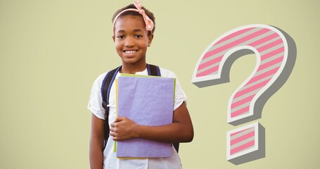 Portrait of smiling schoolgirl holding book by striped question mark over white background
