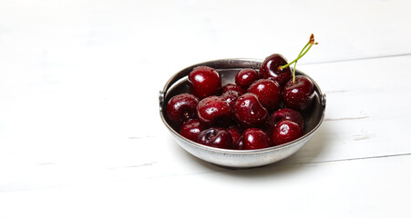 Sweet cherries in a metal bowl on wooden background, closeup. Fresh ripe sweet cherries in a bowl with droplets of water