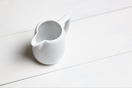 Empty milk jug on wooden background. Porcelain sauce boat, pitcher, creamer or ceramic gravy boat
