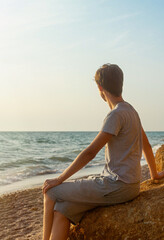 A young man sits on the seashore on a sunny day. Loneliness and social distance concept. Faceless.