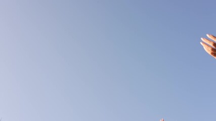 Closeup view 4k slow motion video of two female hands isolated on clear sunny blue sky background. Anonymous woman throwing many yellow dry fall leaves outdoors happily on sunny autumn day