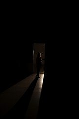 A silhouette of a little girl emerges from a luminous room with smoke in the dark.