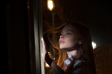 Cute little girl looks at the light from the old window at the old attic. The concept of children's...