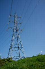 An electricity pylon with multiple cables, carrying high voltahe, on a hill against a blue sky.