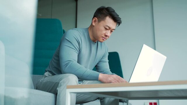 Asian male freelancer working on laptop in modern office coworking center Man student or teacher typing on computer smart professional employee creative, innovative entrepreneur co-working glass space