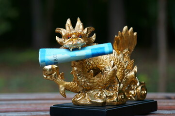 A figurine of a Chinese dragon with money in its teeth in close-up. The symbol of Feng shui. A...