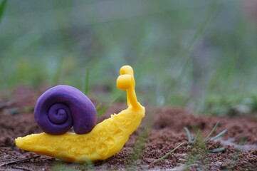 A snail figurine made of plasticine in the green grass. A symbol of spring.