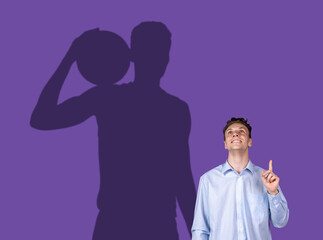 Young man's dreams about big sport future. Conceptual image with man and shadow of strong male basketball player on purple wall