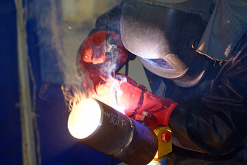 worker welding metal tubes with electrode at a workshop