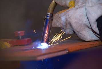 worker hands welding metal plates with semi-automatic welder at a workshop