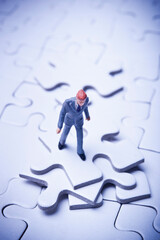 miniature figurine of a businessman standing on a jigsaw puzzle with a missing piece, concept for...