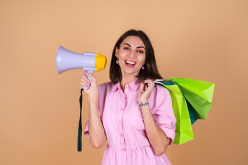 Portrait of a young woman in a pink dress on a beige background with glitter makeup holding shopping packages cute excited shouts into a megaphone