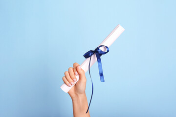 Student holding rolled diploma with ribbon on light blue background, closeup - obrazy, fototapety, plakaty