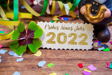 Wooden hang tag and slate with four leaf clover and sparklers with the german words for happy new year - frohes neues jahr 2022 on wooden weathered background
