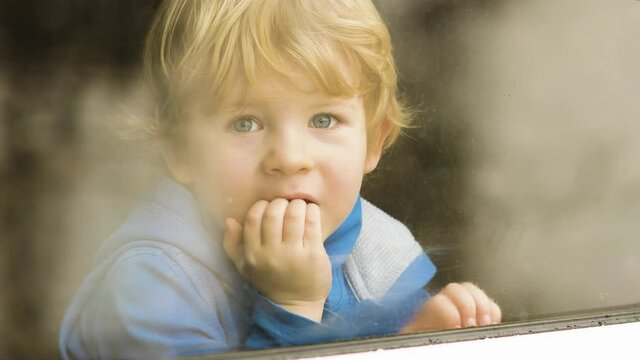 Little blond boy looking out the window while snowfall outside