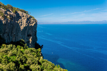 seascape - coastal cliffs in lush tropical vegetation and blue sea with distant mountainous shore