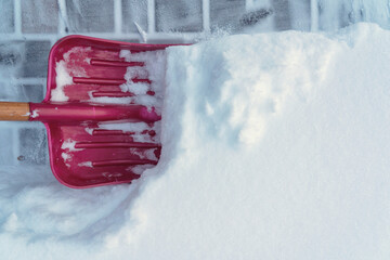A wide red shovel brushes a thick layer of fresh white snow off the cement paving slab. Background....
