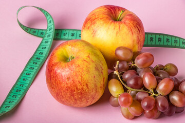 Fresh fruits and measuring tape on a pink background. The concept of diet and healthy eating.