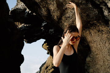 woman in black swimsuit posing near rocks ocean exotic