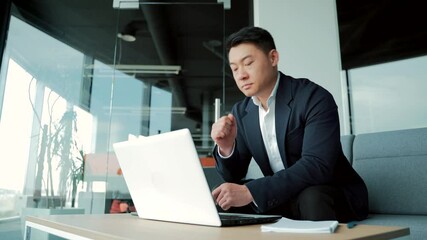Portrait thoughtful Asian businessman working on a laptop computer at a modern office desk. Confident Focused pensive man in formal suit indoors. thinking of inspiration solving a problem. Startup - Powered by Adobe