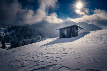 Wooden shed barn on a mountain with a beautiful view over the valleys covered in snow during winter