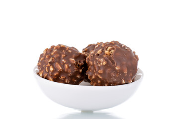 Three sweet chocolate candies with nuts on a white ceramic saucer, close-up, isolated on white.