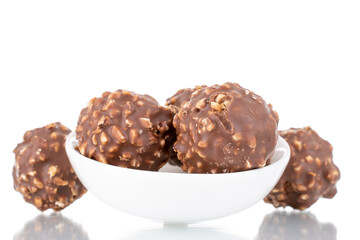 Several sweet chocolate candies with nuts on a white ceramic saucer, close-up, isolated on white.