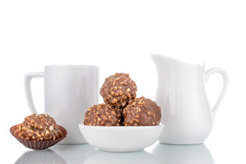 Several sweet chocolate candies with nuts with white ceramic dishes, close-up, isolated on white.
