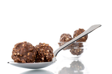 Several sweet chocolate candies with nuts with a metal spoon and a glass plate, close-up, isolated on white.