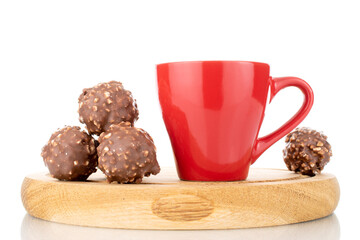 Two sweet chocolates with nuts on a wooden tray with a red cup, close-up, isolated on white.