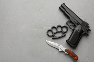 Black brass knuckles, gun and knife on light grey stone background, flat lay. Space for text