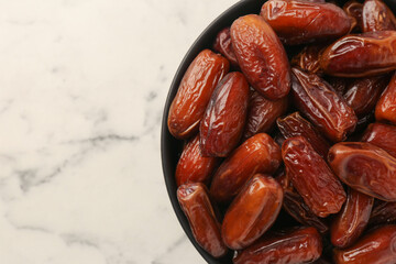 Sweet dried dates in bowl on white marble table, top view. Space for text