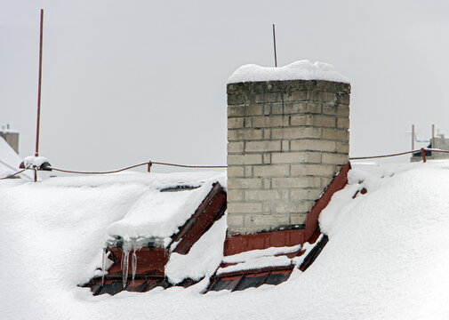 Snow covered roof of house with chimney and skylight.