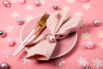 Pink plate, gold cutlery and pink linen napkin on a pink background with Christmas decorations. New Year table setting concept in pink color