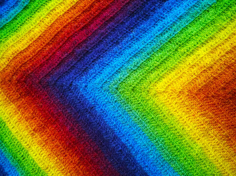Background from gradient of rainbow bright color: burgundy, red, orange, yellow, green, blue, violet, blueberry. Beauty of geometry. Triangles, multi-colored stripes lines. Crocheted fabric. DIY.