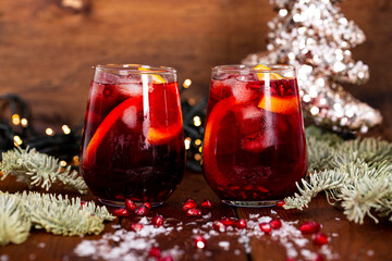 Two glasses of pomegranate cocktail with orange on the background of Christmas decorations and lights. Festive winter drink