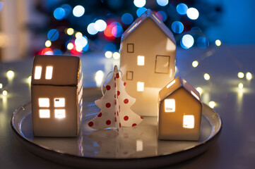 Fototapeta premium Little Scandinavian hauses, Christmas tree, and magic bokeh lights on background