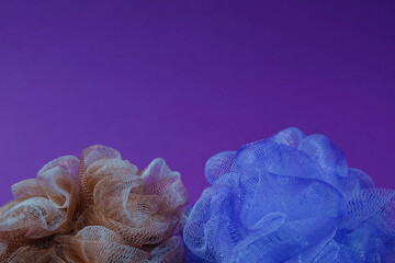 Blue and light brown mesh bath sponge on a violet background. Text space. Hygiene, decoration,...