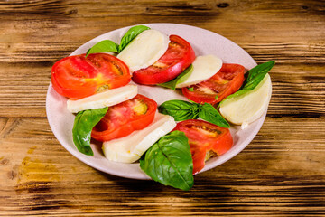 Plate with caprese salad (italian salad with cherry tomatoes, mozzarella cheese and basil leaves) on wooden table