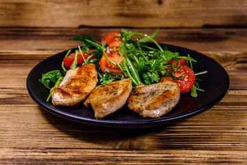 Roasted chicken breasts and salad with arugula and cherry tomatoes in a black plate