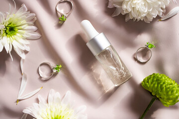 Obraz na płótnie Canvas A transparent bottle with a natural cosmetic product on a pastel pink background with natural flowers. Skin care concept. Flat lay.