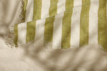 Striped linen beach towel with fringes on sandy beach with shadows from palm tree. Relaxation and...